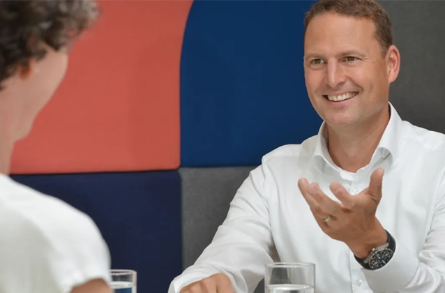 Zwei Personen reden mit einander, eine Person lächtelt und gestukuliert mit den Händen. 